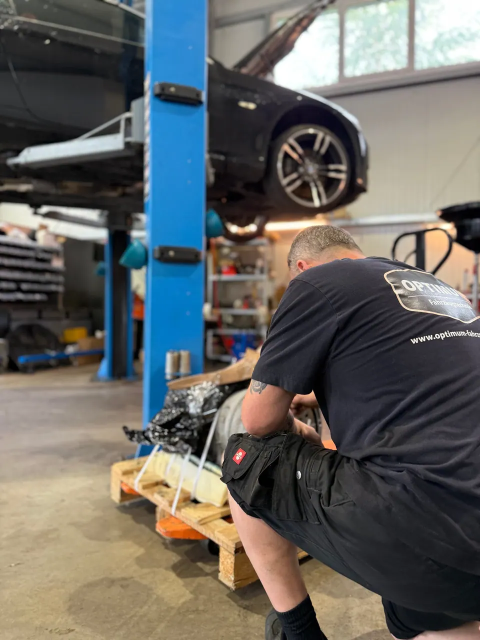 Optimum Mechaniker in schwarzem Shirt arbeitet unter Auto auf Hebebühne